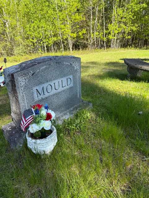 American flag beside an arrangement at an upright headstone
